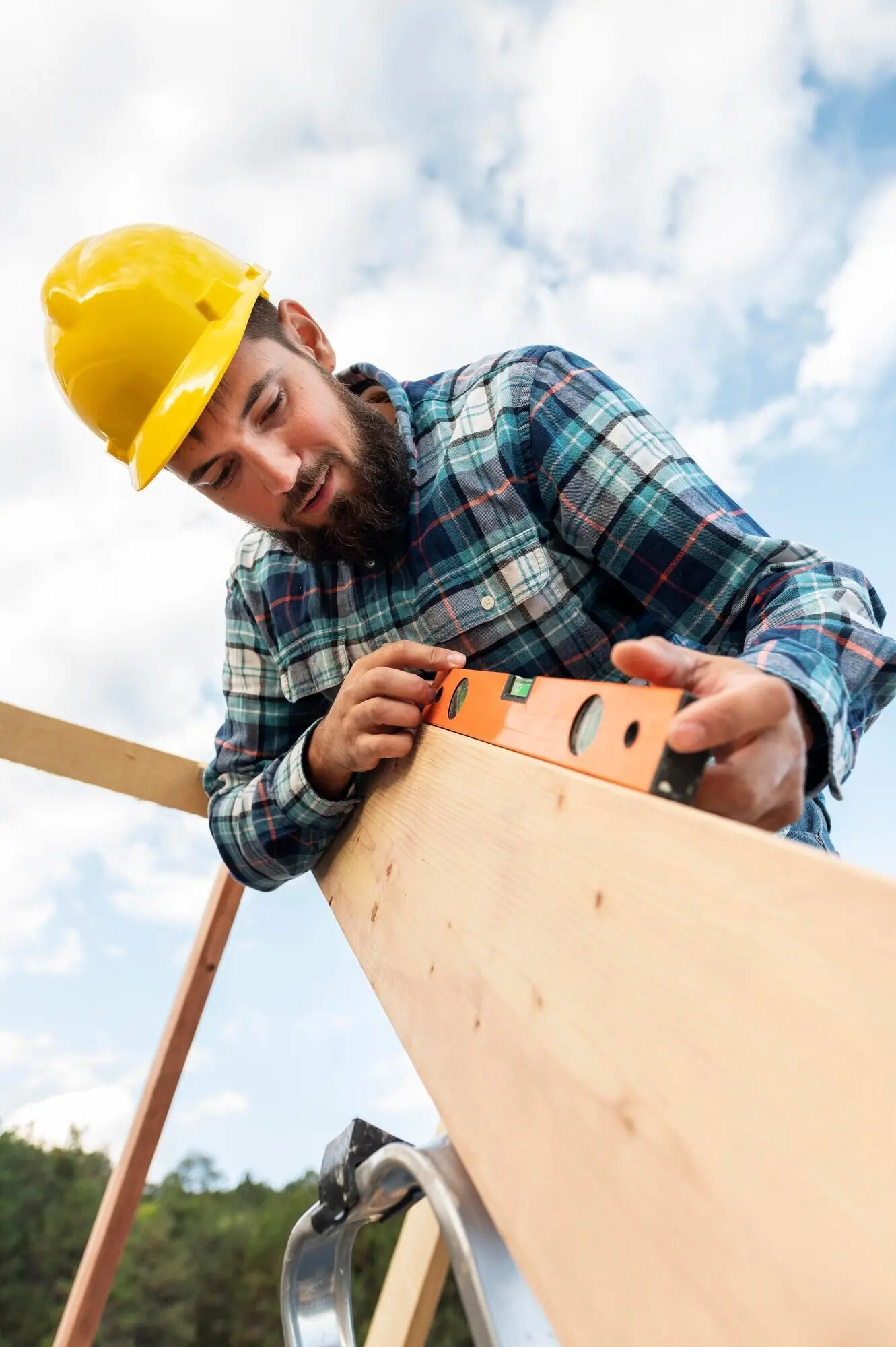 A worker wearing a hard hat checks the roof timber with a level.